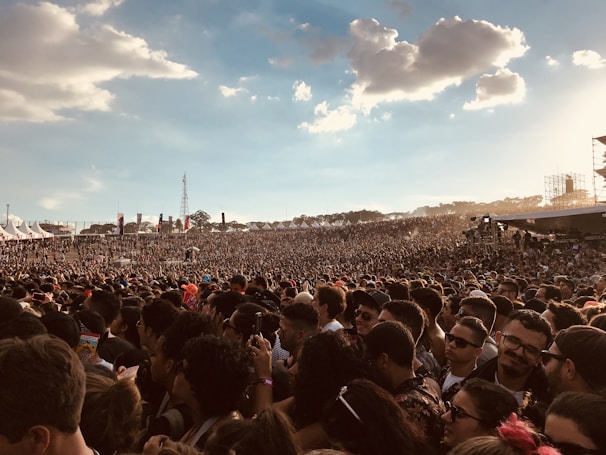 A lively crowd cheering at a packed outdoor music festival under a clear sky.
