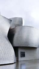 a large grey building with Guggenheim Museum Bilbao in the background