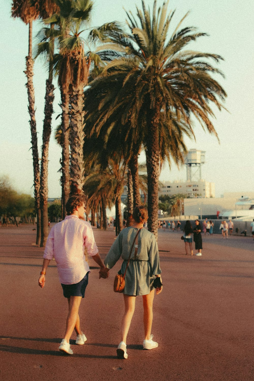 a couple of people walking on a street with palm trees