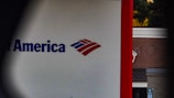 A partial view of a sign, displaying a recognizable red, white, and blue logo. The words 'of America' are visible, suggesting it is associated with a financial institution. The background shows a building with a brick facade.
