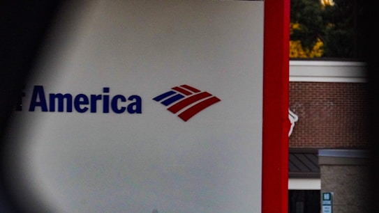 A partial view of a sign, displaying a recognizable red, white, and blue logo. The words 'of America' are visible, suggesting it is associated with a financial institution. The background shows a building with a brick facade.