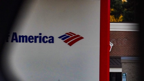 A partial view of a sign, displaying a recognizable red, white, and blue logo. The words 'of America' are visible, suggesting it is associated with a financial institution. The background shows a building with a brick facade.