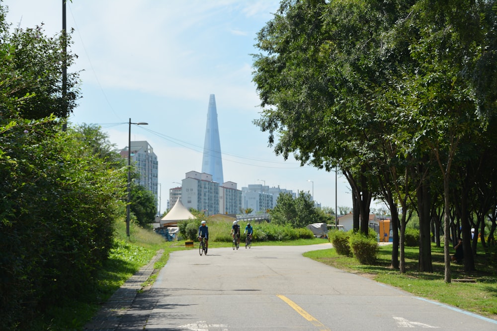 a group of people riding bikes on a road with trees and buildings in the background