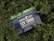 A lithium battery labeled 'NEWPOWA LITHIUM 12V 100Ah 1280 Wh LiFePO4 BATTERY' is surrounded by lush green foliage.