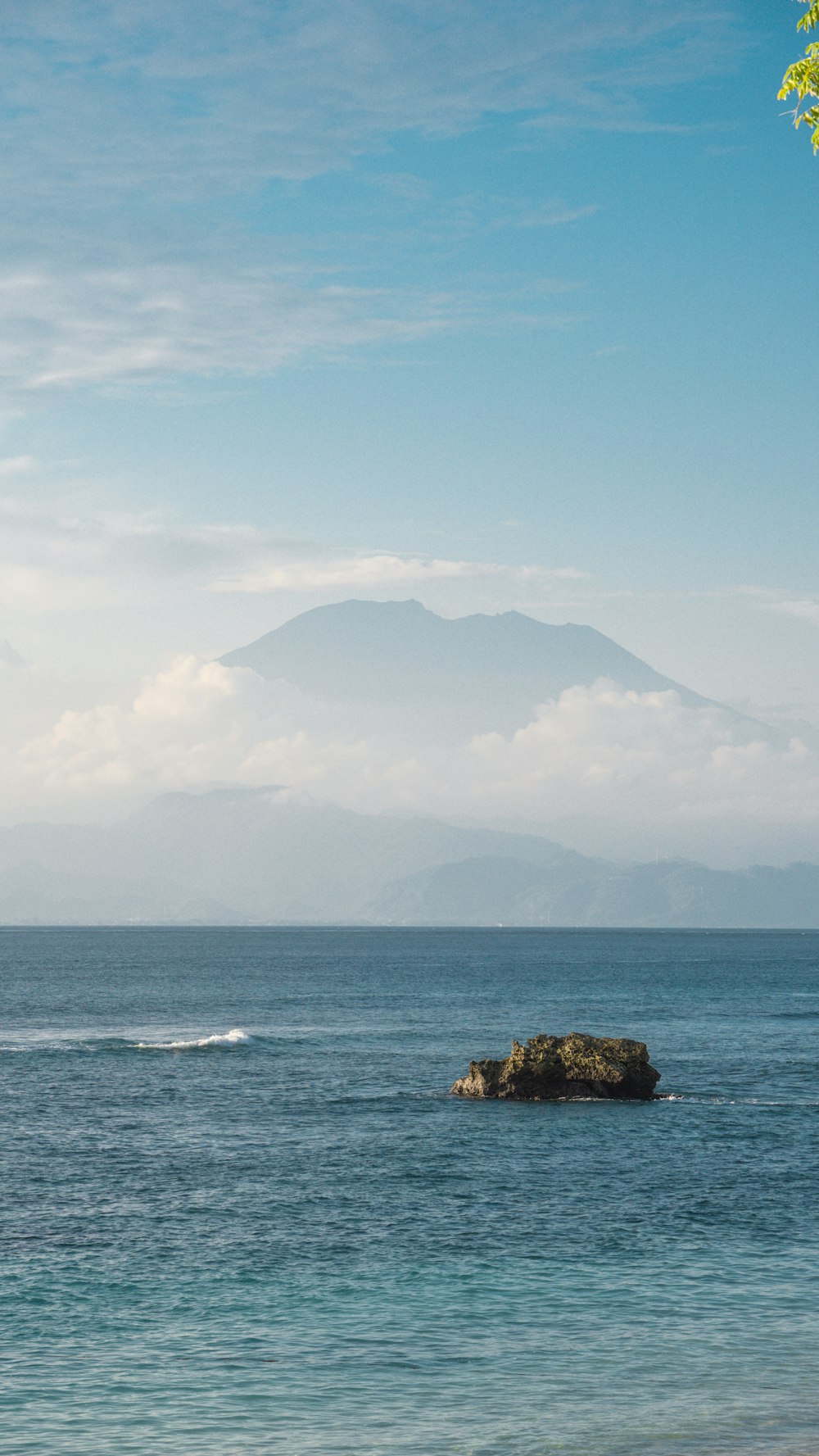 a rock in the middle of the water with a mountain in the background