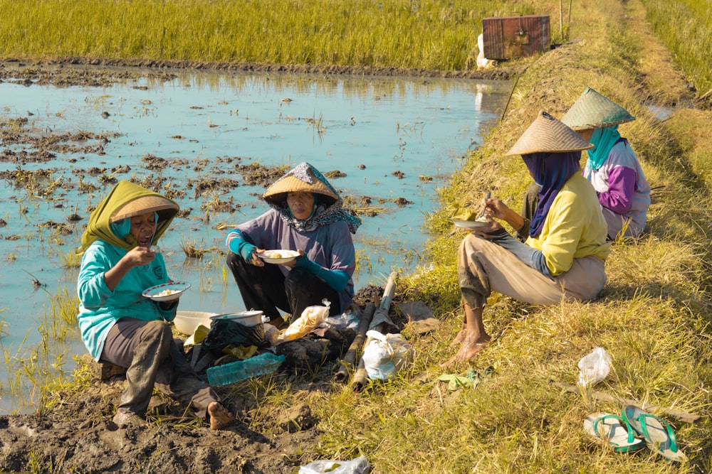 a group of people sitting by a river with hats on