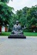 a statue of a man sitting on a stone bench in a park