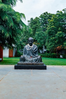 a statue of a man sitting on a stone bench in a park