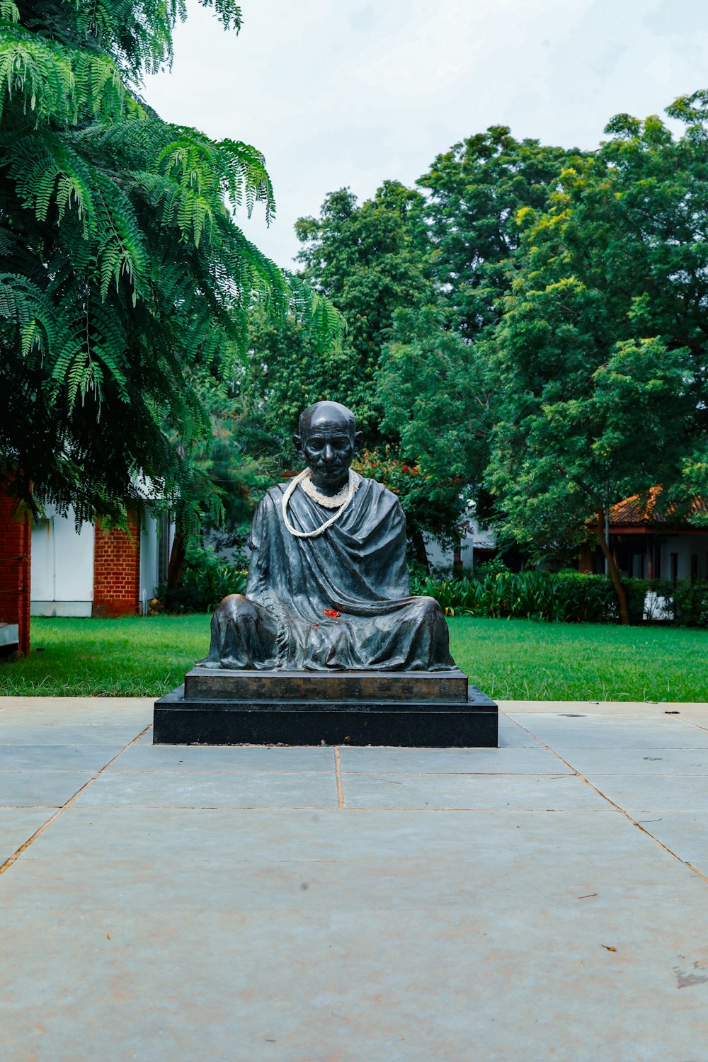 a statue of a man sitting on a stone bench in a park