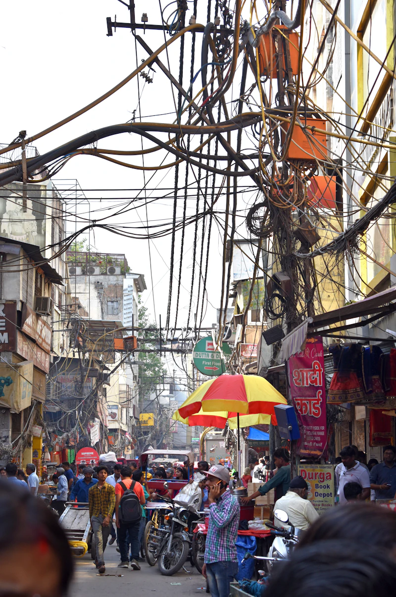 A busy bazaar street in Old Delhi crowded with people and umbrellas