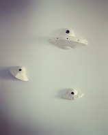 White ceramic objects resembling UFOs are mounted on a light gray wall. They vary in size and have a minimalist, modern design with a central black dot.