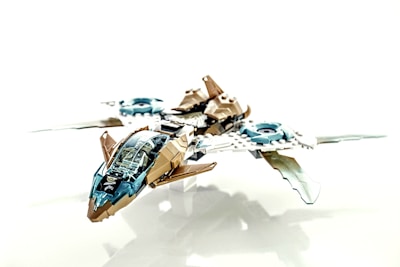 A detailed, futuristic toy spaceship made from interlocking plastic bricks, featuring blue and beige colors with transparent elements for the cockpit. The design includes sleek wings and intricate mechanical details, giving it a sci-fi appearance.