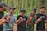 A group of five young men are standing in a forest, holding hands and laughing together. They are dressed casually and appear to be enjoying each other's company amidst the tall trees.