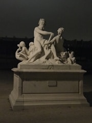 An antique-style handcrafted sculpture displayed on a wooden pedestal.