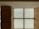 A modern interior with wooden walls and a large, backlit textured glass window panel divided into four sections by cross-shaped framework. The glass features intricate circular patterns, and the wood has a smooth, warm finish.