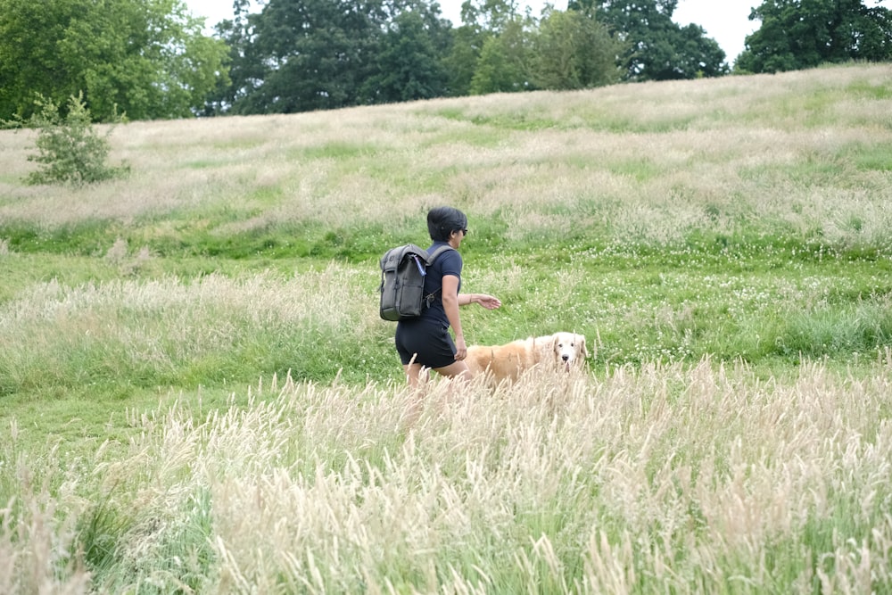 una persona con uno zaino che porta a spasso un cane in un campo erboso