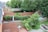 Aerial view of a backyard area featuring multiple fenced sections with trees and greenery. A playground set is visible in one section, while another section contains a swimming pool. Patio furniture is arranged on a stone-tiled area and a pergola structure is adjacent to the house.
