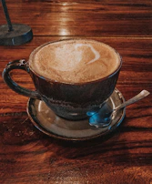 A steaming cup of coffee beside a golden spoon on a white marble table.