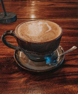 A steaming cup of coffee beside a golden spoon on a white marble table.