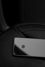A smartphone lies face down on a textured black leather surface, showcasing its camera and fingerprint sensor.