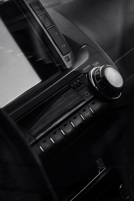 A close-up view of a car dashboard featuring an audio control unit with buttons and a large knob. The design is sleek with a modern look, and there is a small screen above the controls.