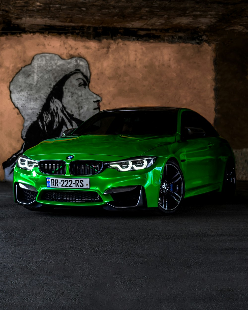 a green car parked in front of a wall with a picture of a person on it