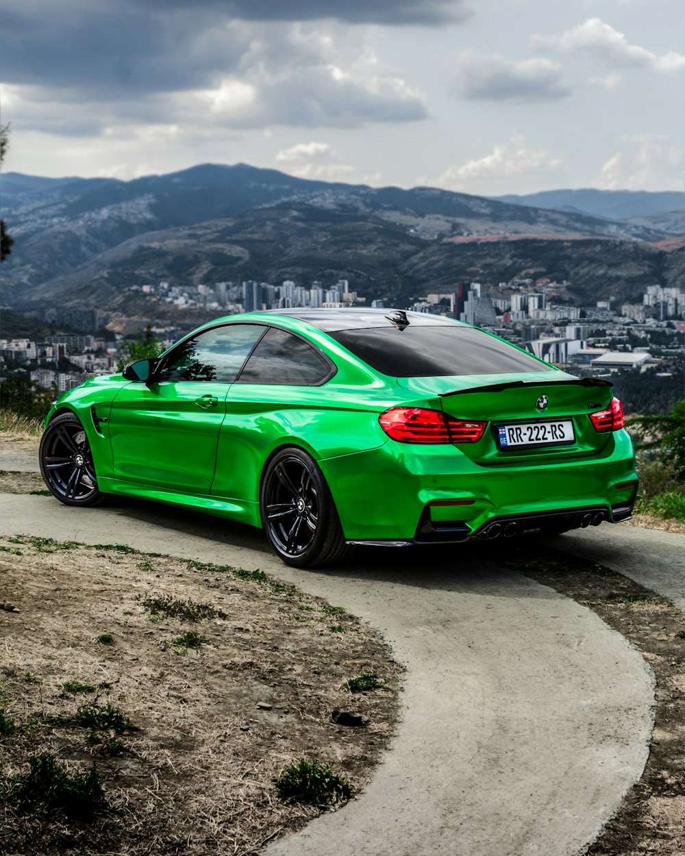 a green car parked on a dirt road with hills in the background