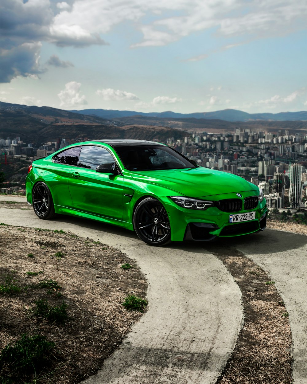 a green car parked on a road with a city in the background