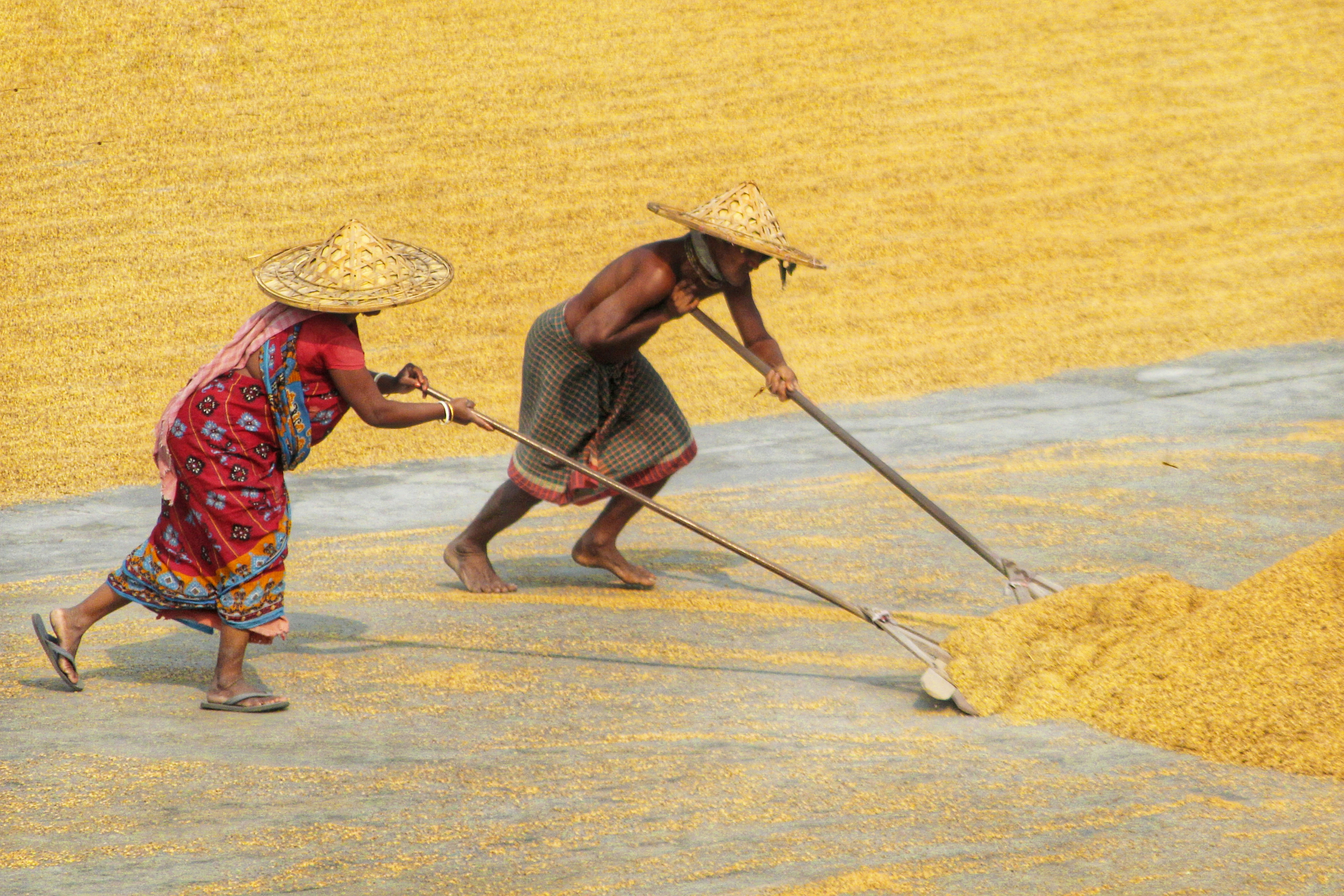 a man and woman walking on a road with a broom and hat