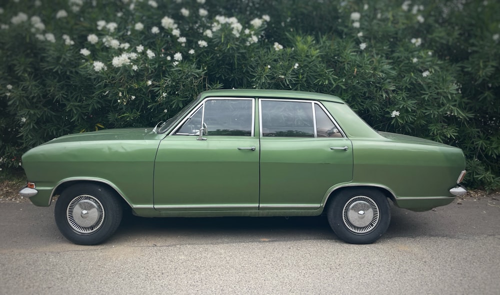 a green car parked in front of a bush