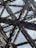 Intricate metallic structures form an elaborate network of beams and girders, creating an architectural design with geometric patterns. The beams appear sturdy and are set against a backdrop of a cloudy sky.