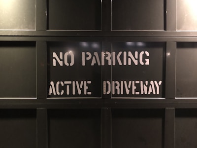 Metal garage door with the text 'NO PARKING ACTIVE DRIVEWAY' stenciled in white, placed within a grid-like pattern formed by the door's panels.