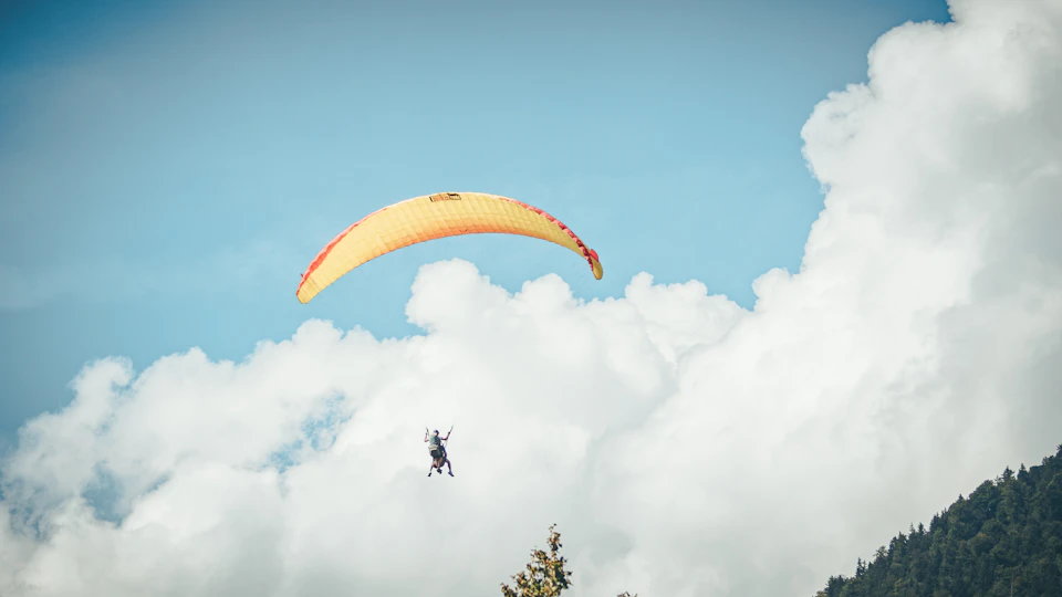 Person paragliding with unfurled parachute soaring high above mountain range