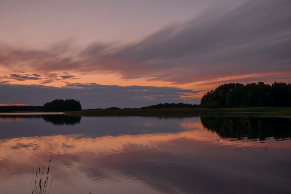 a body of water with trees and a sunset in the background