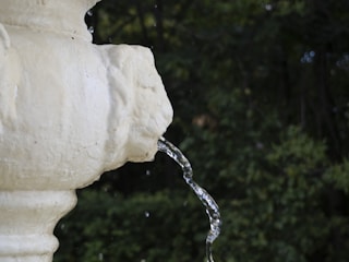 A modern stone fountain with flowing water set in a garden background.