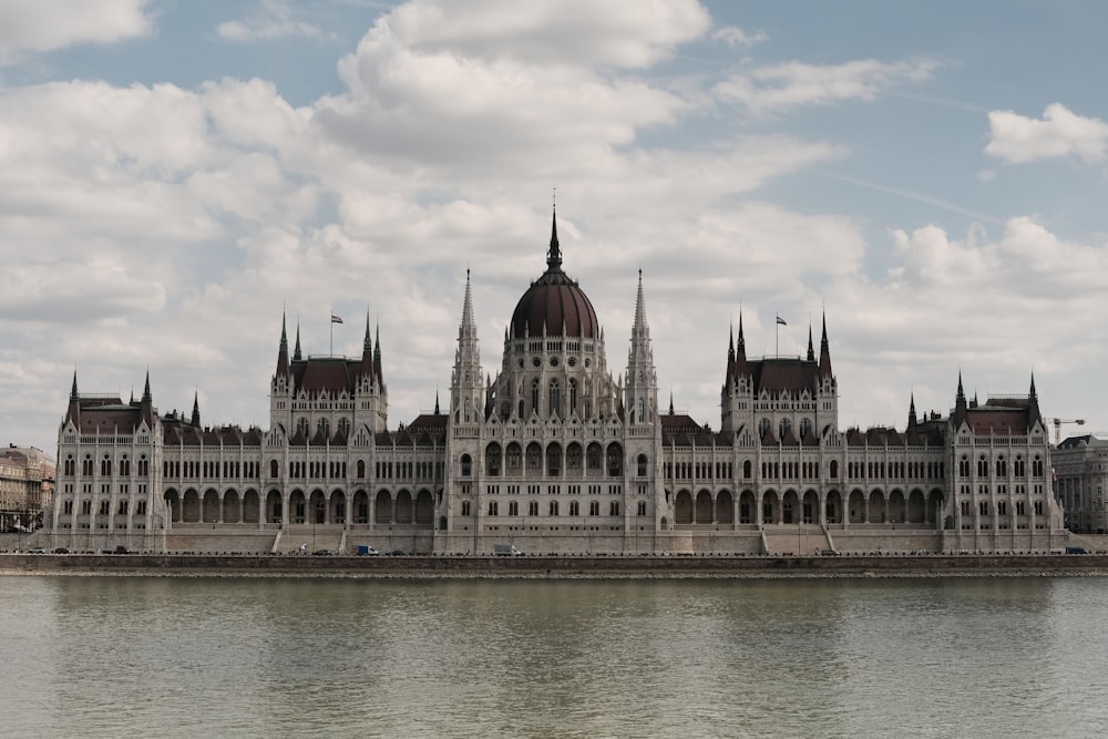 a large white building with a domed roof by a body of water with Hungarian Parliament Building in the background