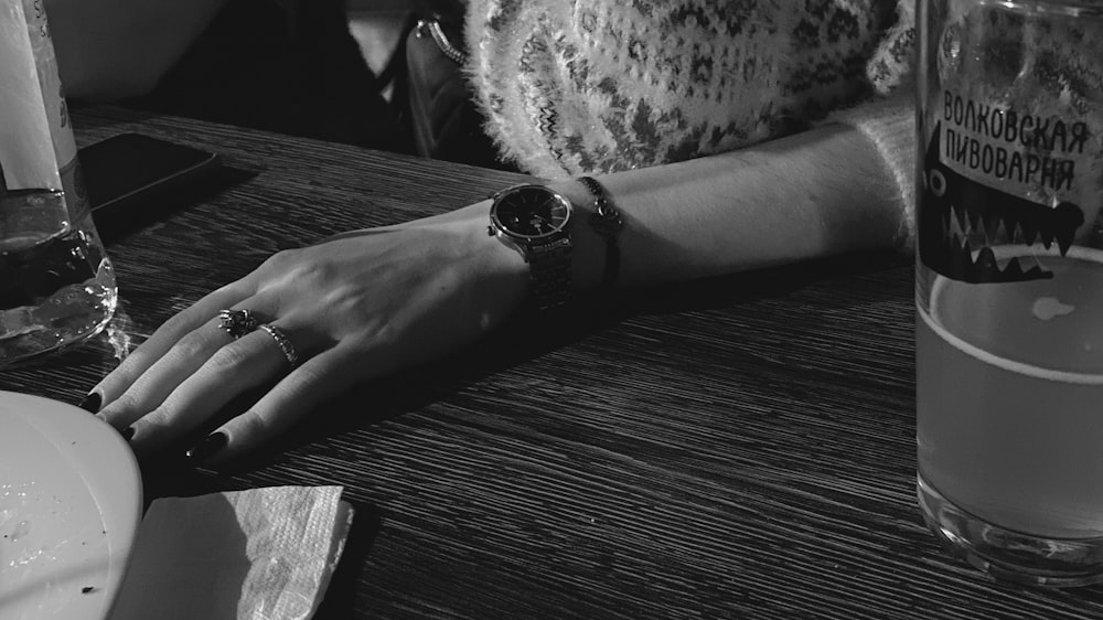 a person's hand on a table with a glass of beer