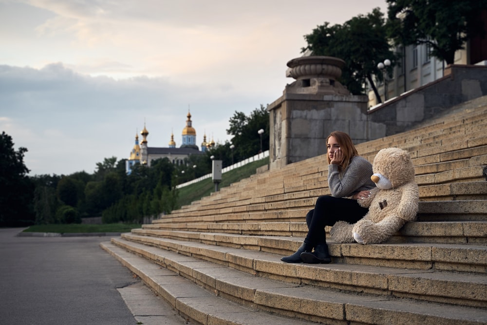 a person sitting on a stone staircase with a teddy bear