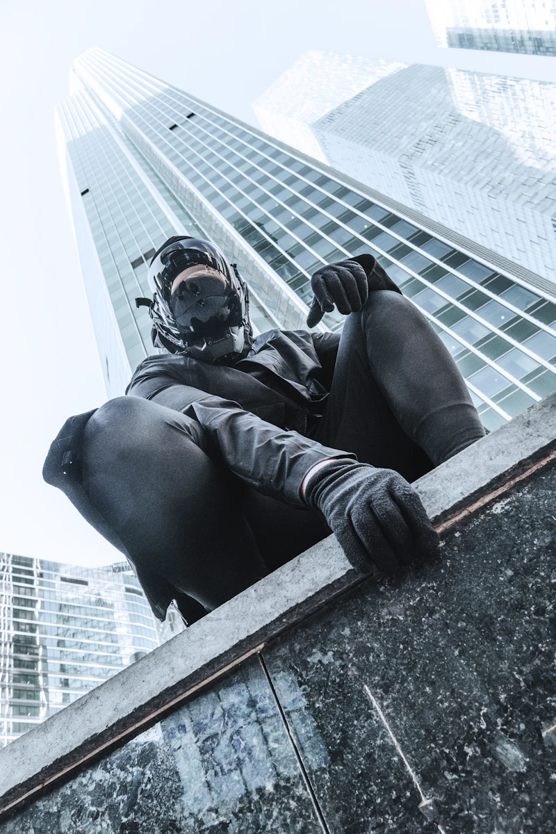 Model in black technical gear perched on a glass tower ledge