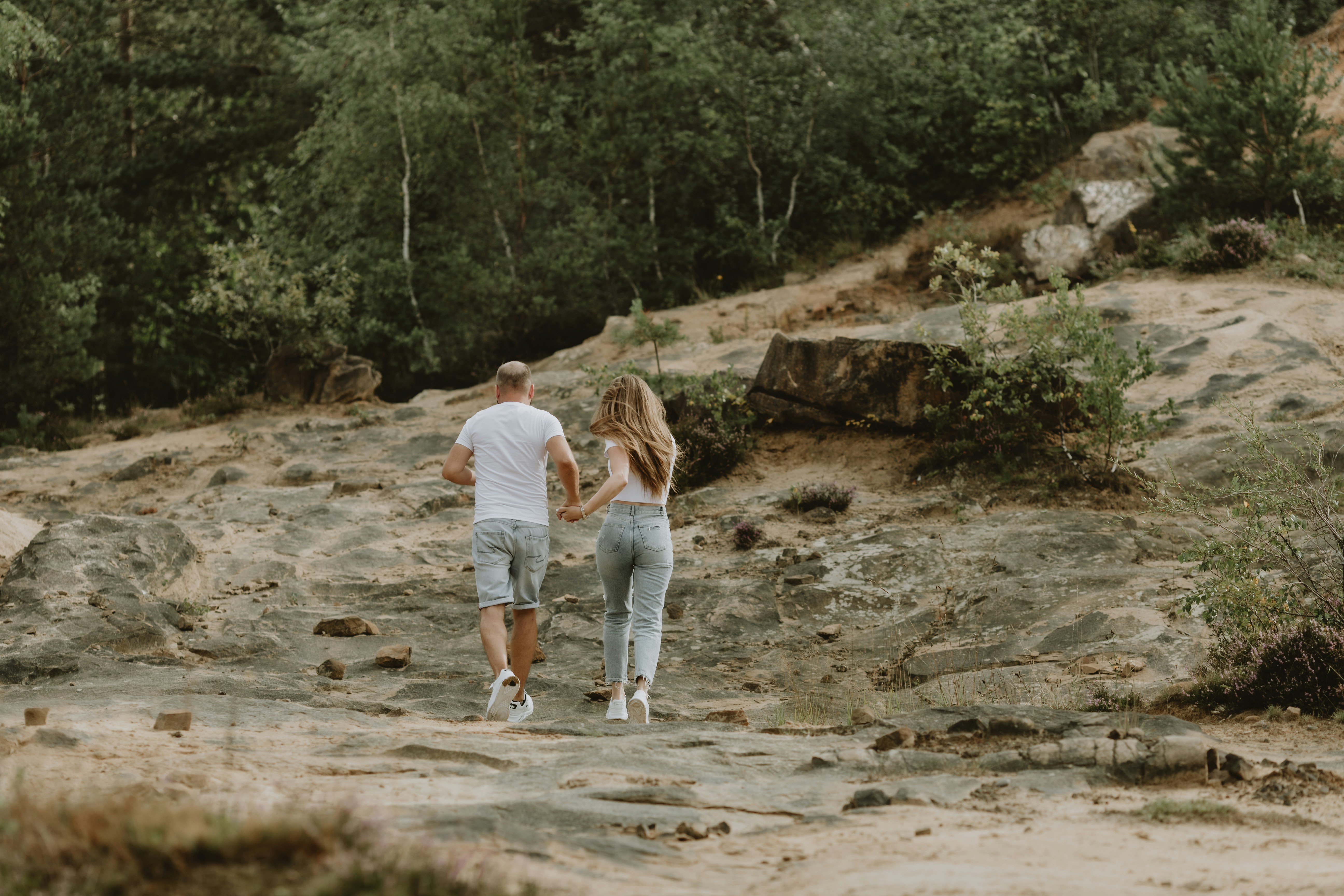 a man and woman walking on a dirt path in the woods