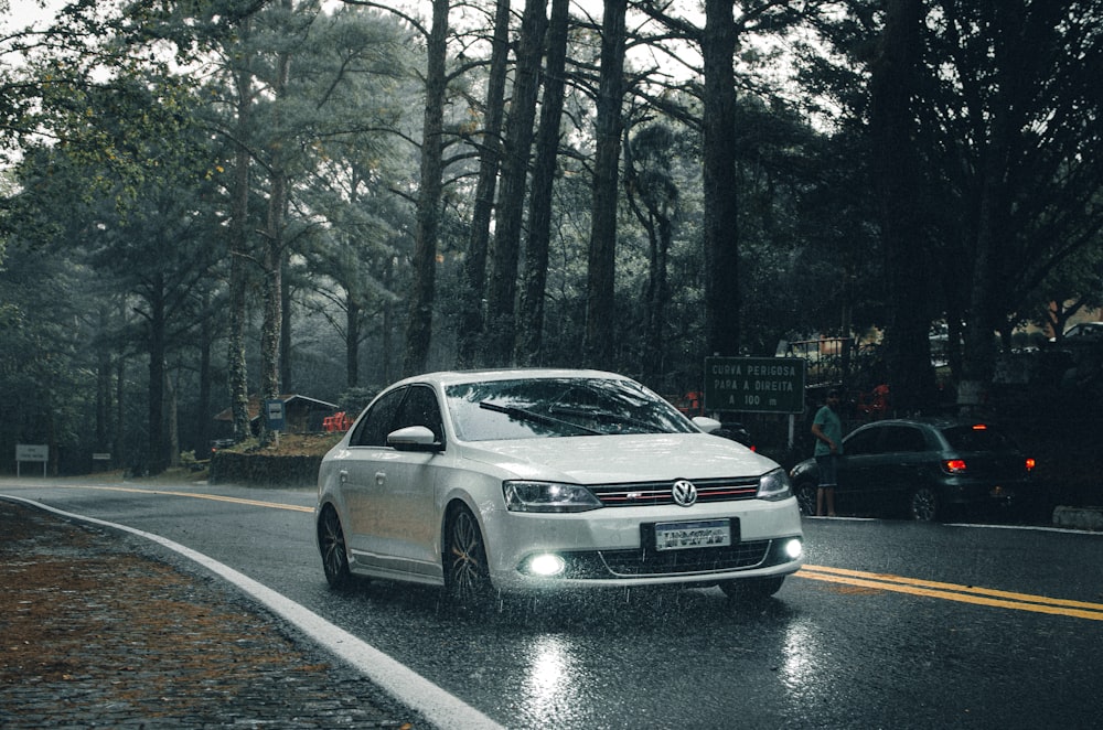 a white car on a road with trees on either side of it