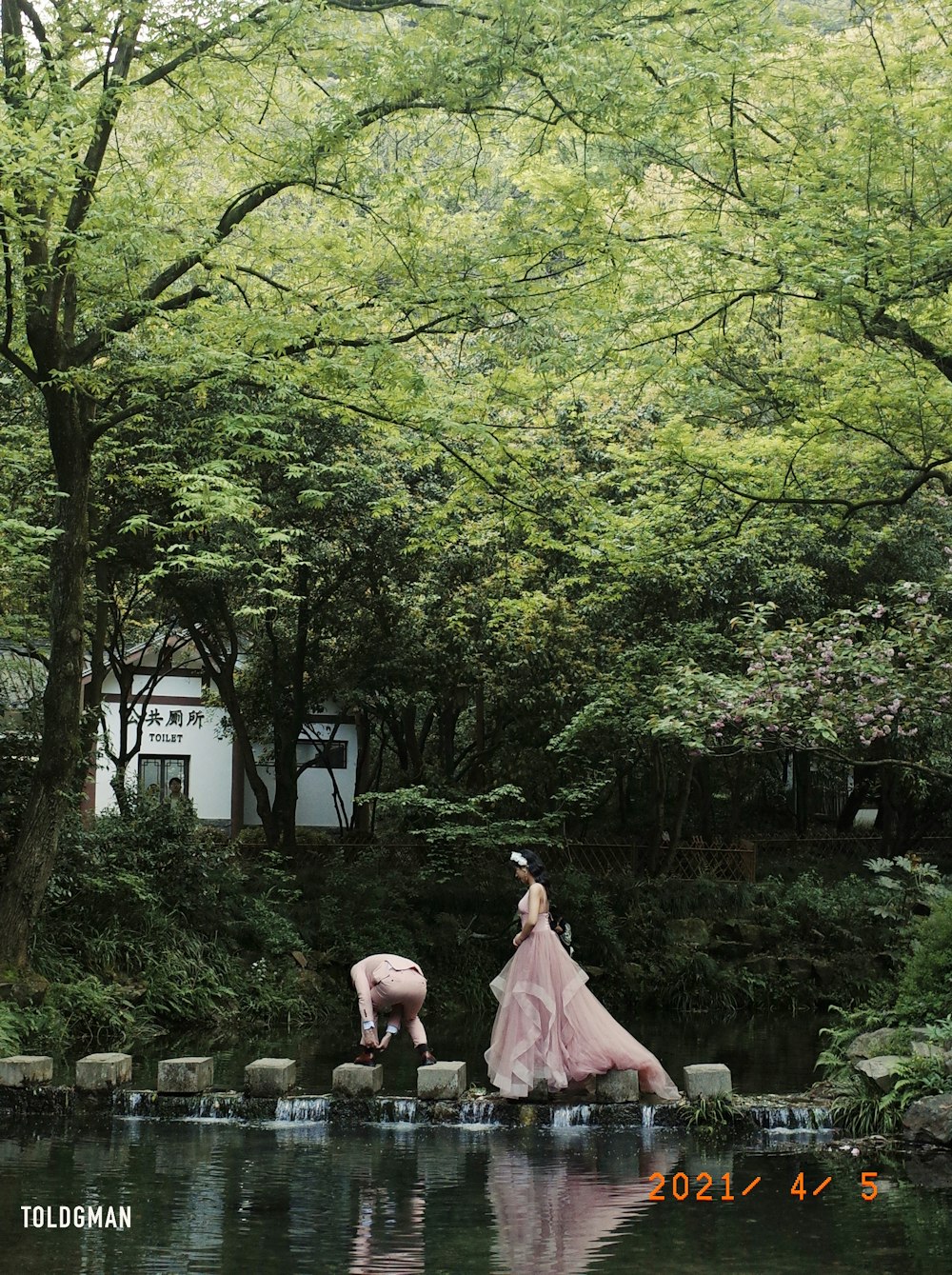 a person in a pink dress standing in water with trees and a building in the background