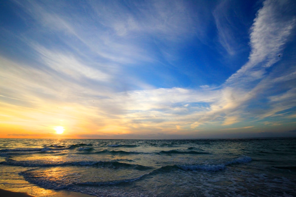 a beach with waves and the sun setting