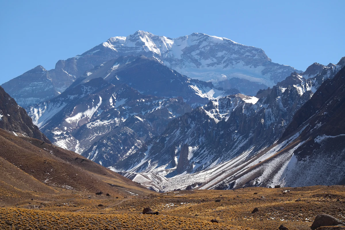 The snow-streaked south face of Aconcagua rises above the golden Horcones valley under a clear blue sky.