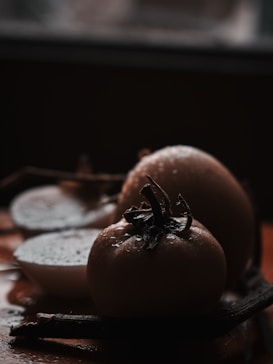 A close-up image of ripe persimmons with droplets of water on their surface, creating a fresh and natural feel. The fruits are positioned against a dark, blurred background, highlighting their details and texture.