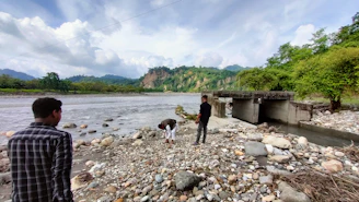 Field geologists collecting soil and water samples near a riverbank.