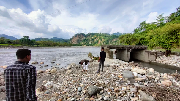 Field geologists collecting soil and water samples near a riverbank.
