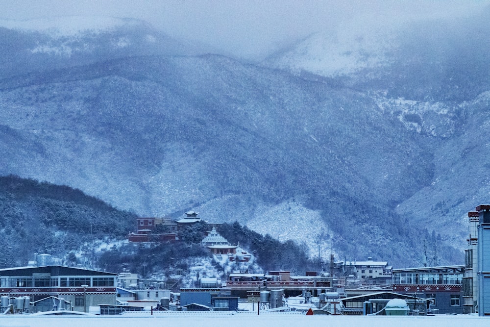 a group of buildings with snow on the roofs and mountains in the background