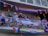 A group of people stand on a balcony decorated with colorful Pride flags and banners. The decorations include rainbow patterns and messages promoting love and gender inclusivity. Some people are leaning on the railing, engaging in conversation, and wearing accessories that match the vibrant theme.