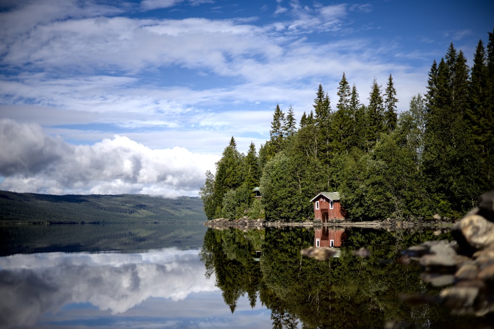 a building on a hill by a lake with trees and clouds in the sky